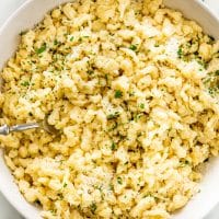 overhead shot of spaetzle in a white bowl topped with parsley and parmesan cheese with a fork inside