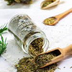 an herb jar on its side spilling italian seasoning on a table with a little scoop scooping some up