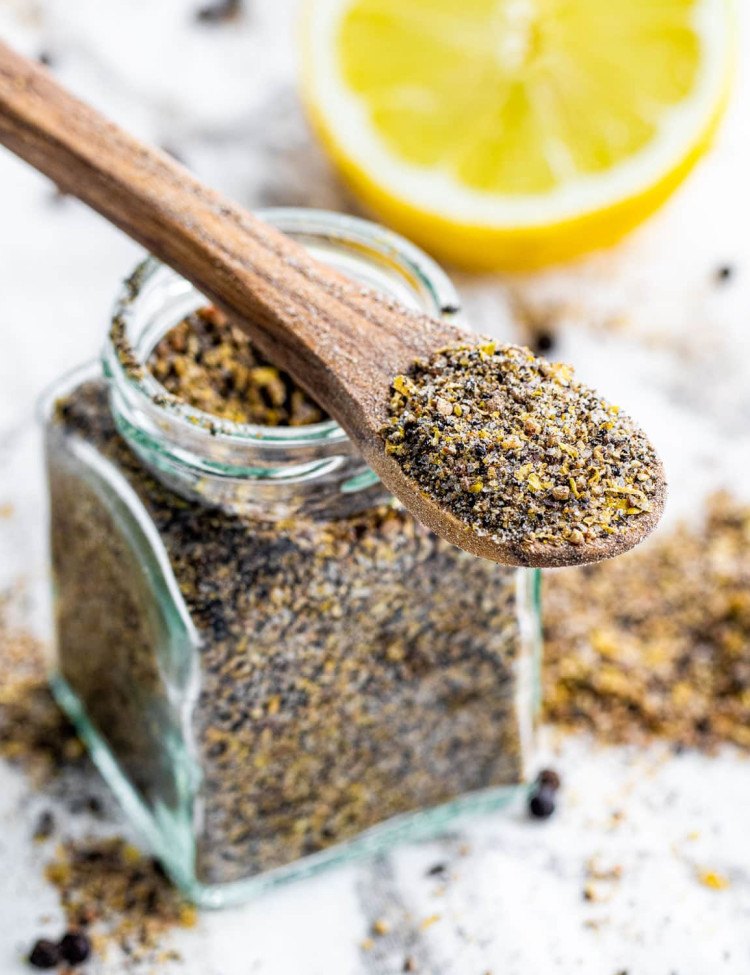 a jar with freshly made lemon pepper seasoning and a tiny wooden spoon with a bit of spice on it hanging on the jar