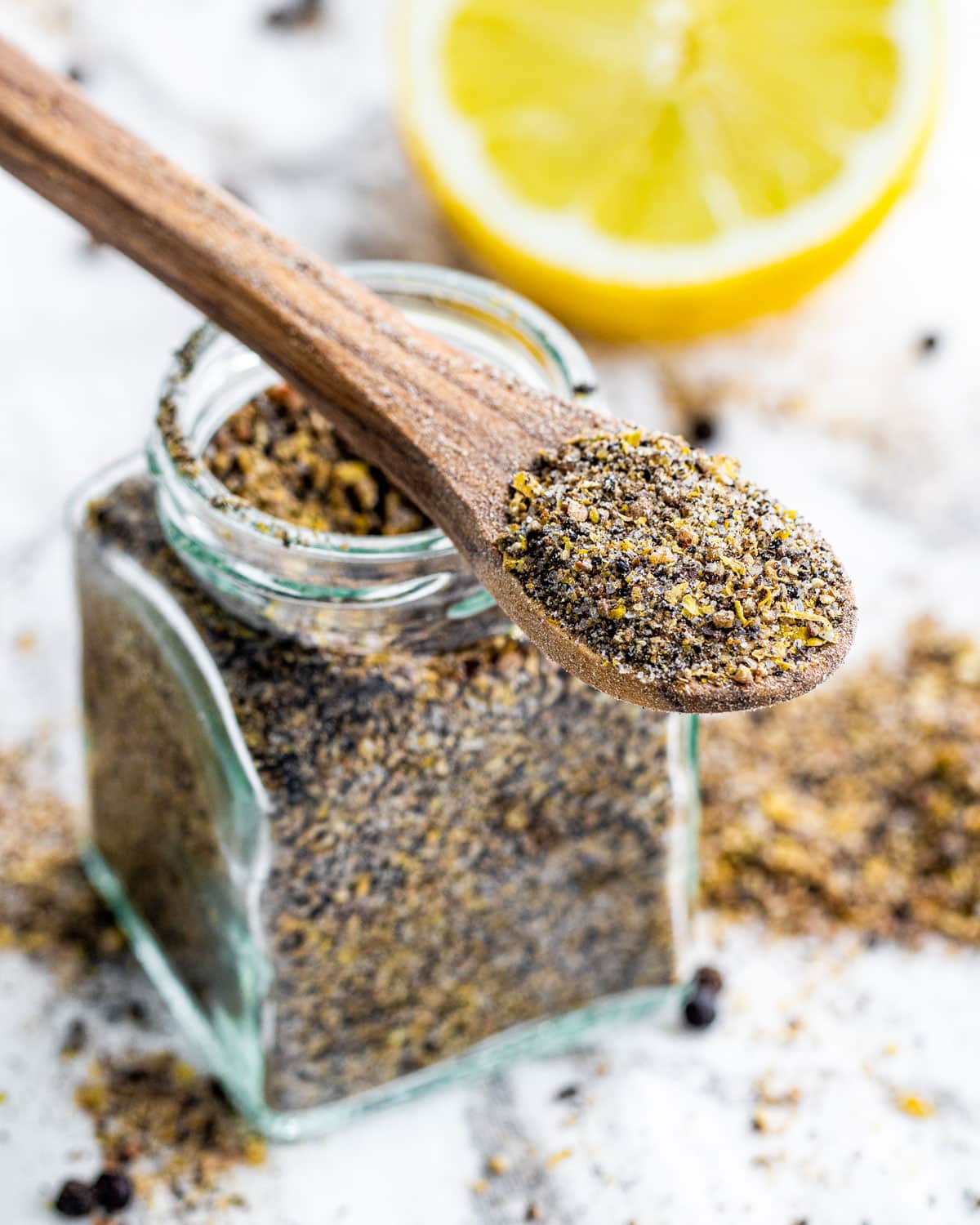 a jar with freshly made lemon pepper seasoning and a tiny wooden spoon with a bit of spice on it hanging on the jar