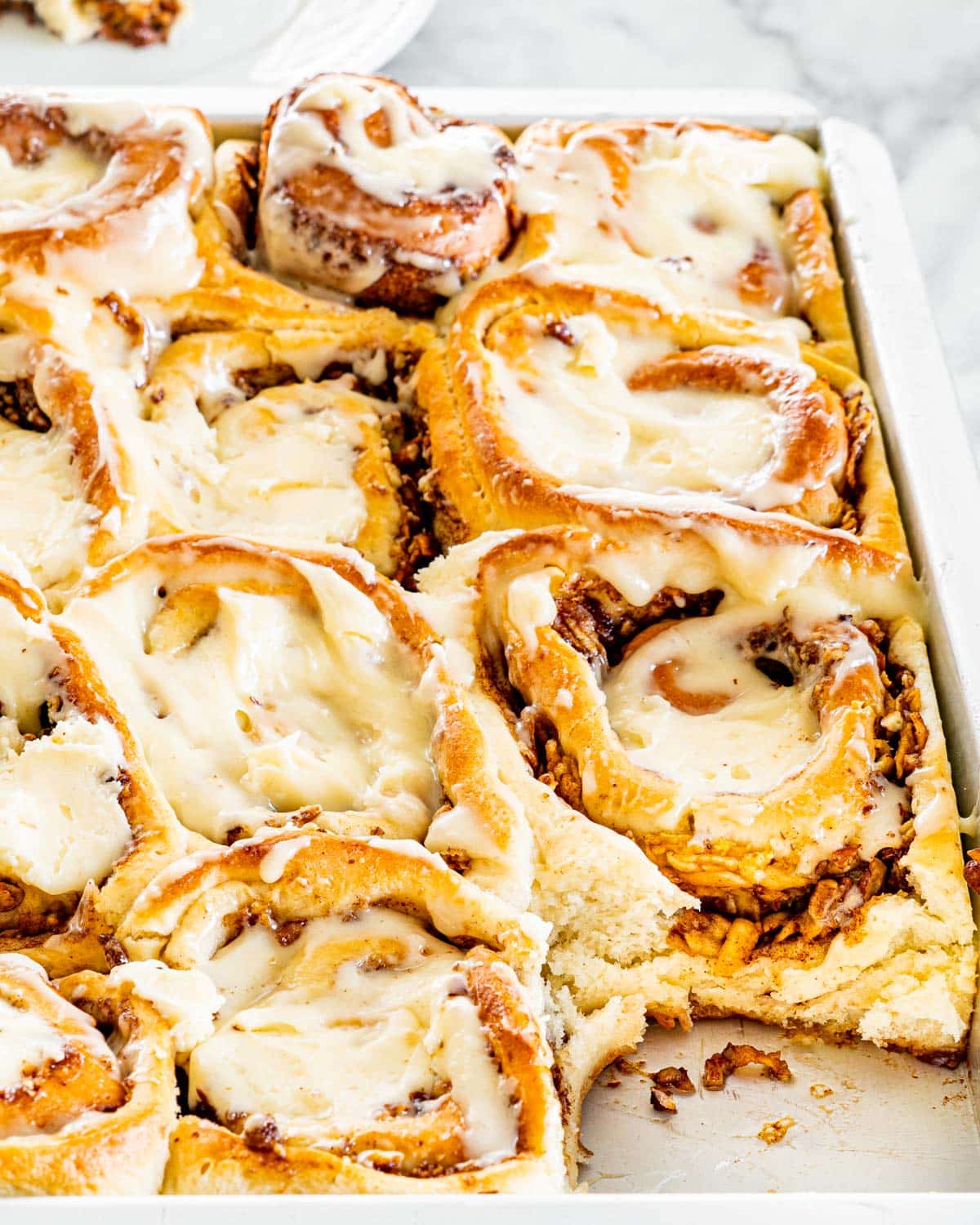 side shot of apple pecan cinnamon rolls in a baking pan, iced with cream cheese icing with a roll missing