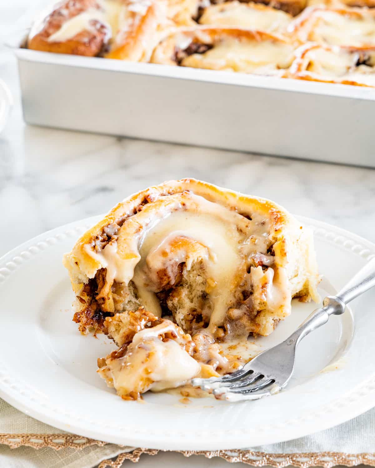 an apple pecan cinnamon roll with on a white plate with a fork on the plat and a bite taken out of the roll