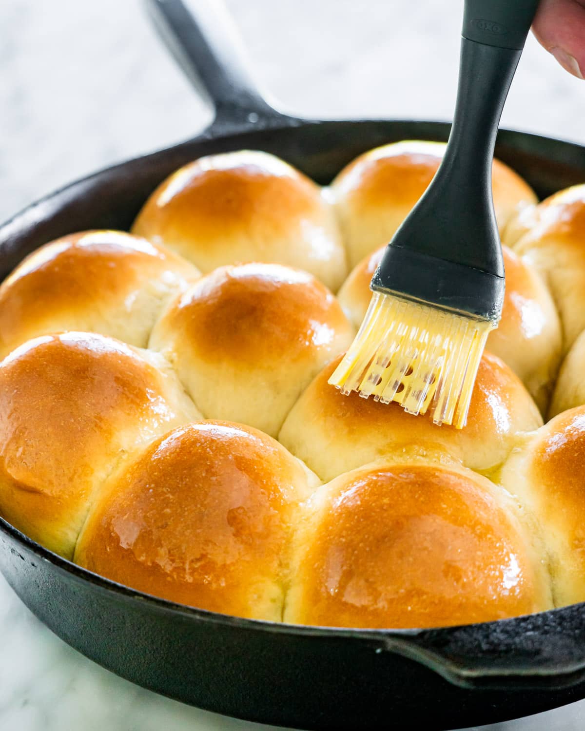 a hand brushing belted butter over dinner rolls that were just baked in a skillet