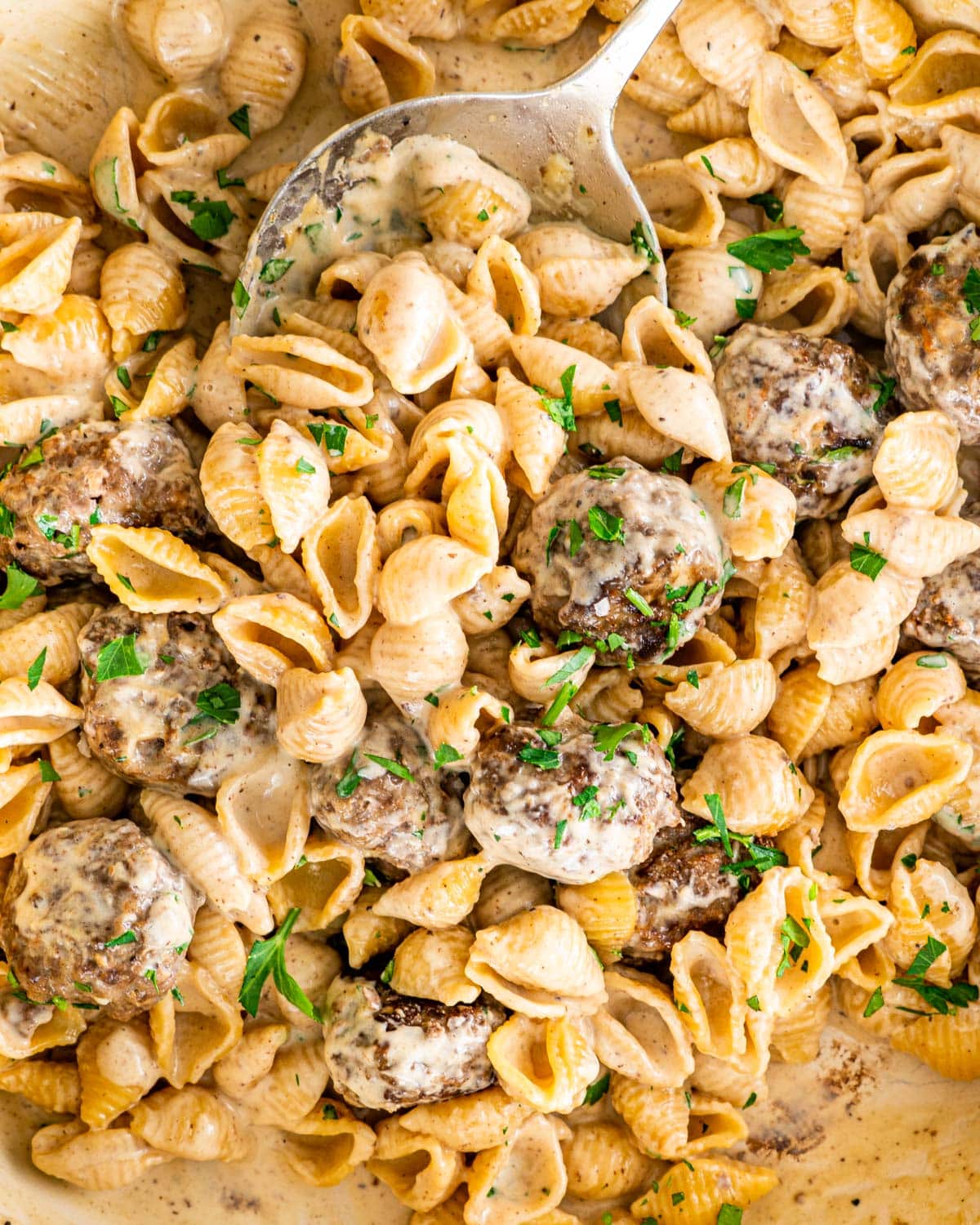 overhead close up shot of swedish meatball pasta in a beige braised garnished with parsley