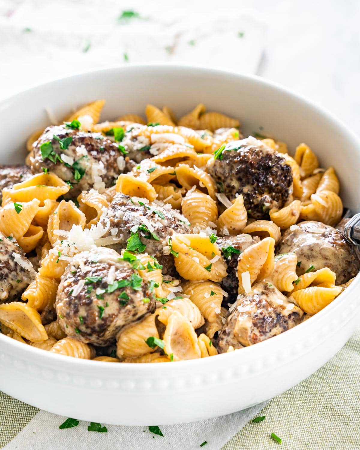 side shot of swedish meatball pasta in a small white bowl garnished with parmesan cheese and parsley