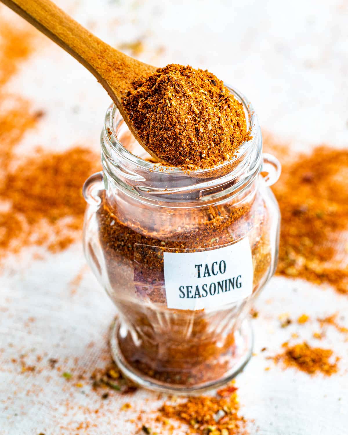 a small spice jar filled with taco seasoning and a mini wooden spoon spooning some out