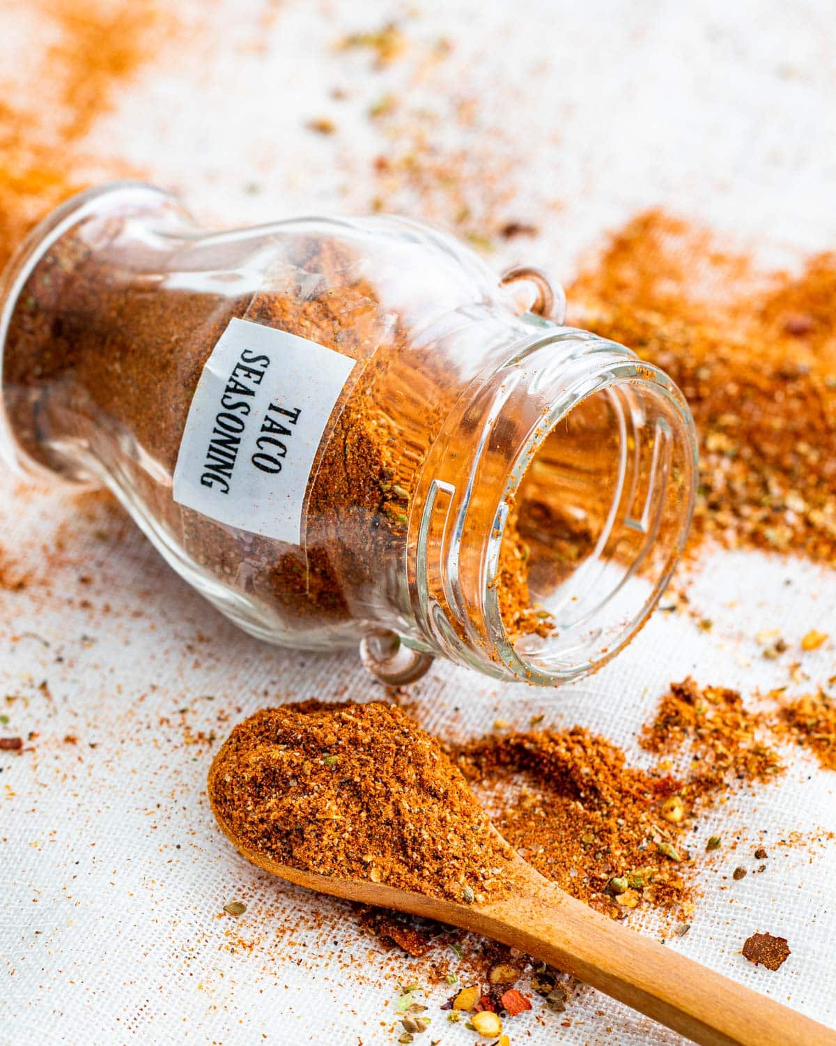 a small spice jar on its side with taco seasoning inside and a mini wooden spoon next to it