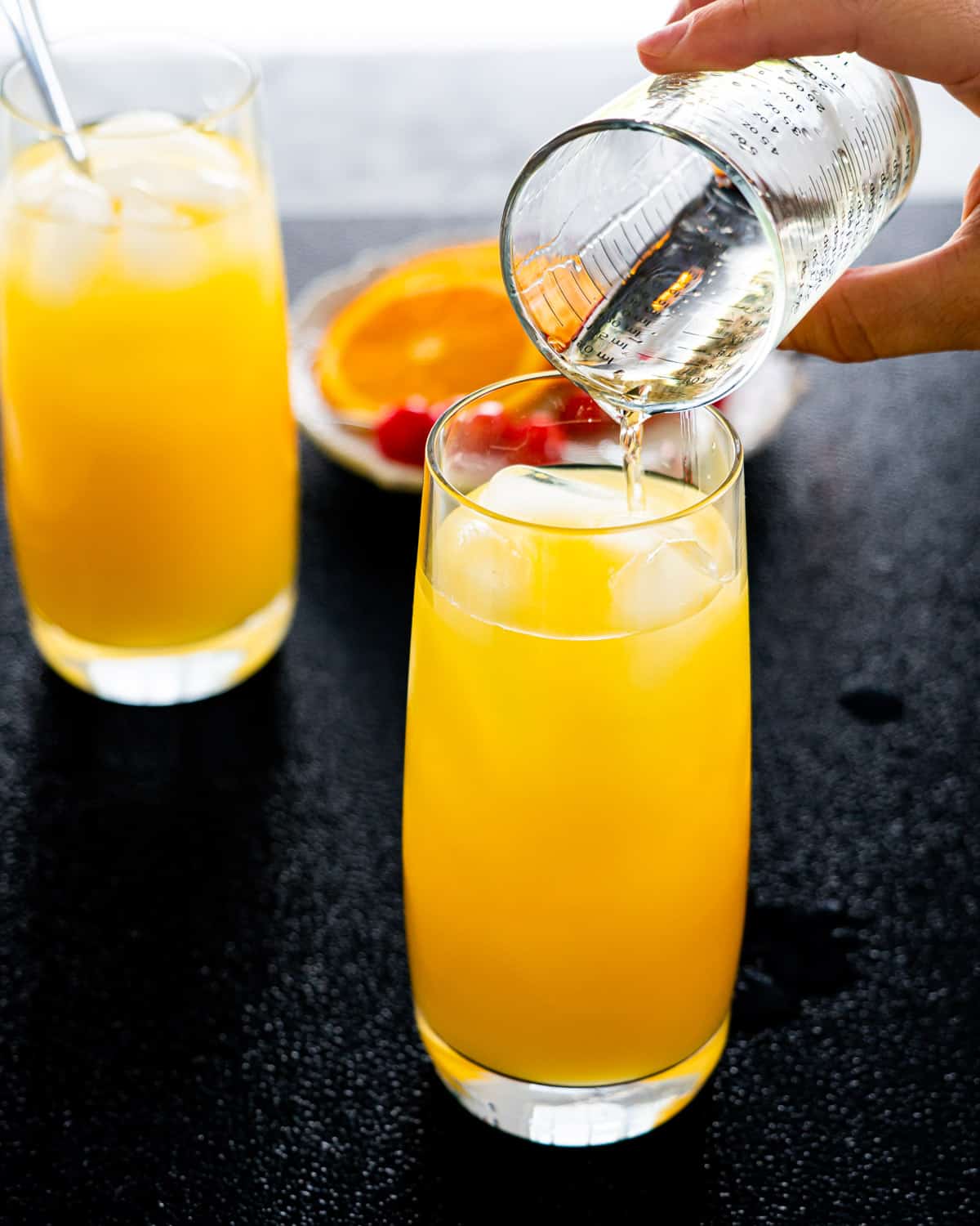 a hand pouring tequila in a glass full with orange and ice
