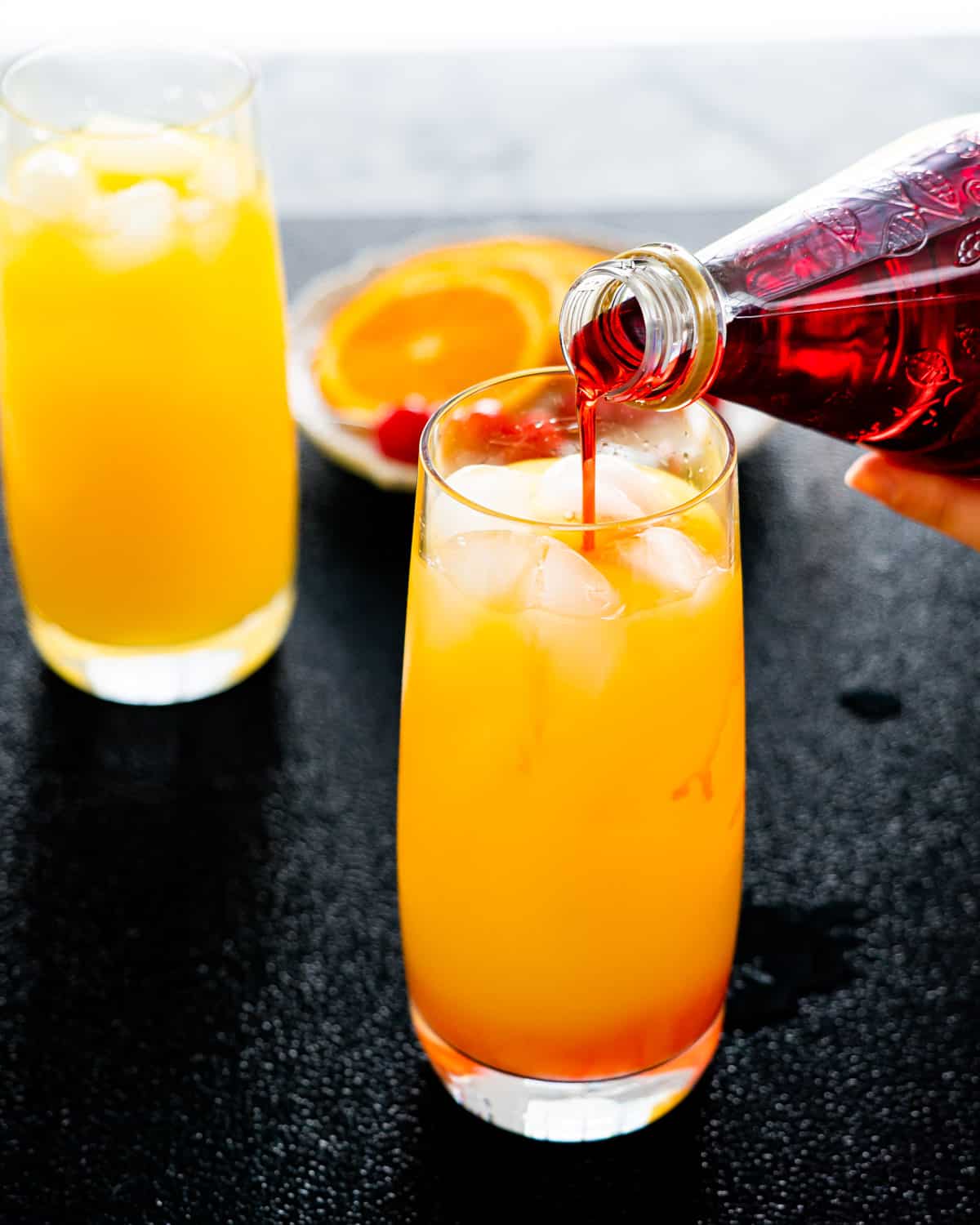 pouring of grenadine in a glass with orange and tequila to make tequila sunrise