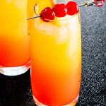 two glasses with tequila sunrise garnished with orange and maraschino cherries