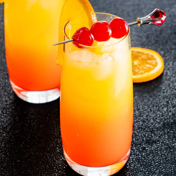 two glasses with tequila sunrise garnished with orange and maraschino cherries