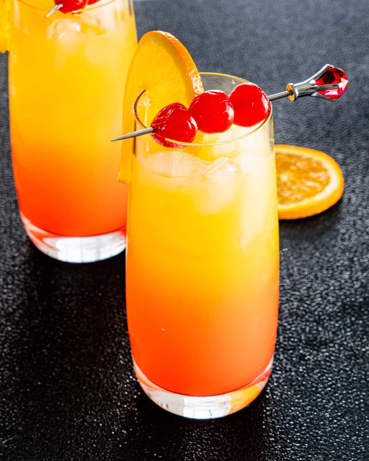 two glasses with tequila sunrise garnished with orange and maraschino cherries