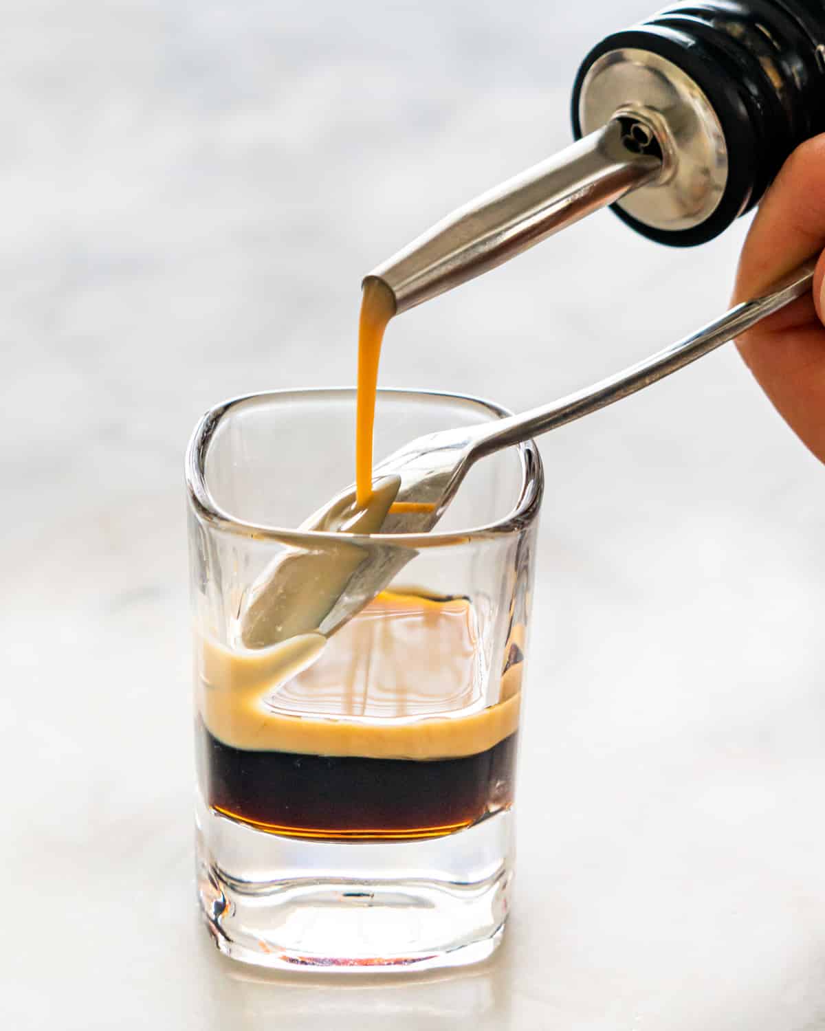 side view shot of pouring irish cream over a teaspoon in a shot glass with a coffee liqueur layer