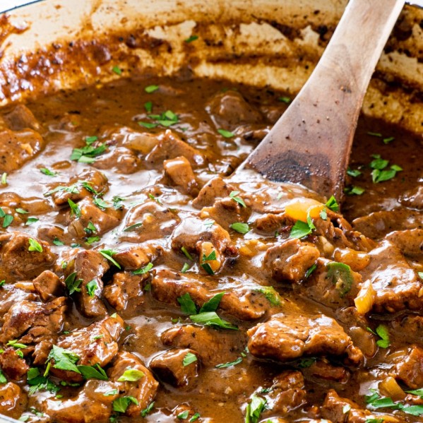 closeup shot of beef tips with gravy in a pot with a wooden spoon inside