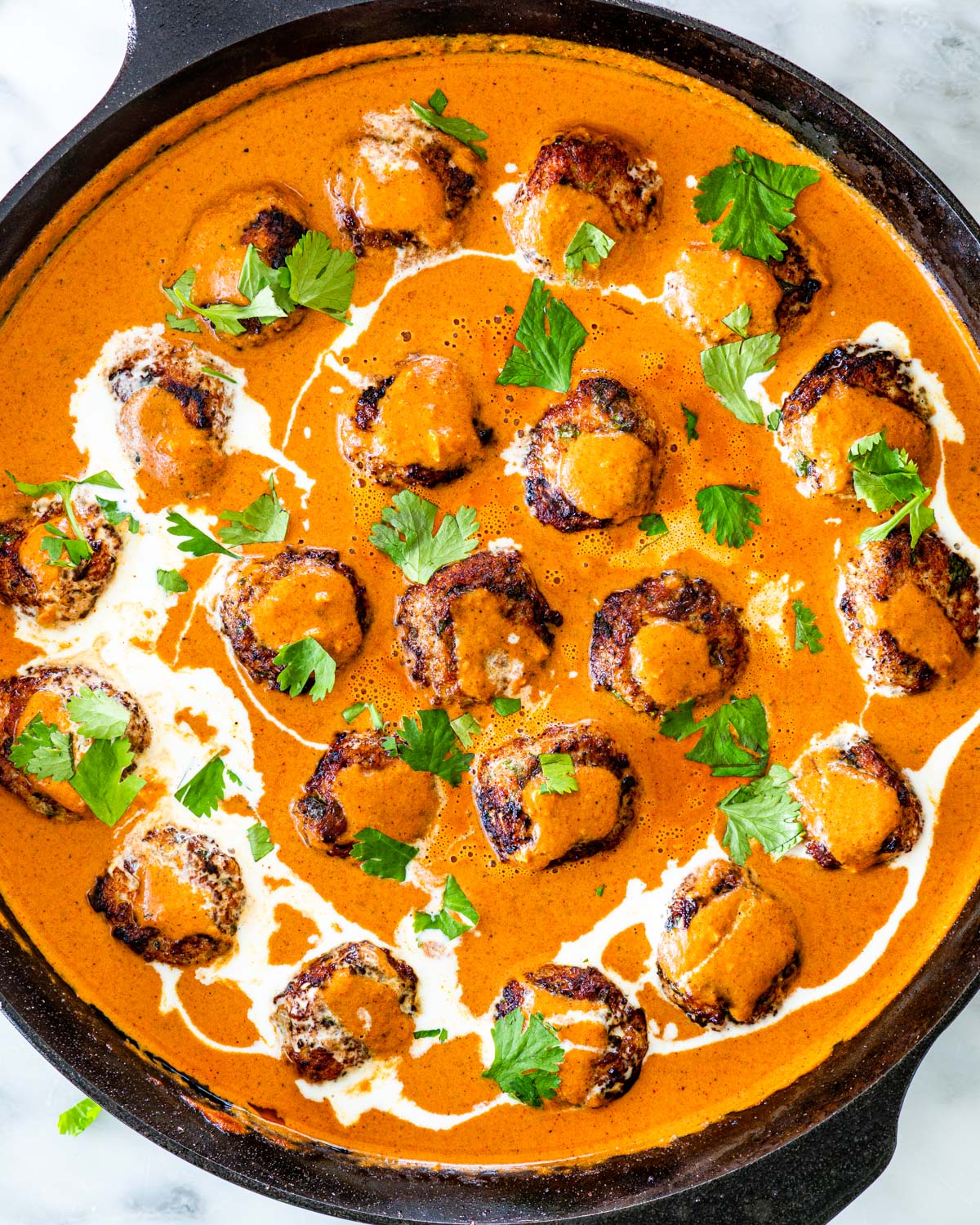 overhead shot of butter chicken meatballs in a black skillet garnished with cilantro