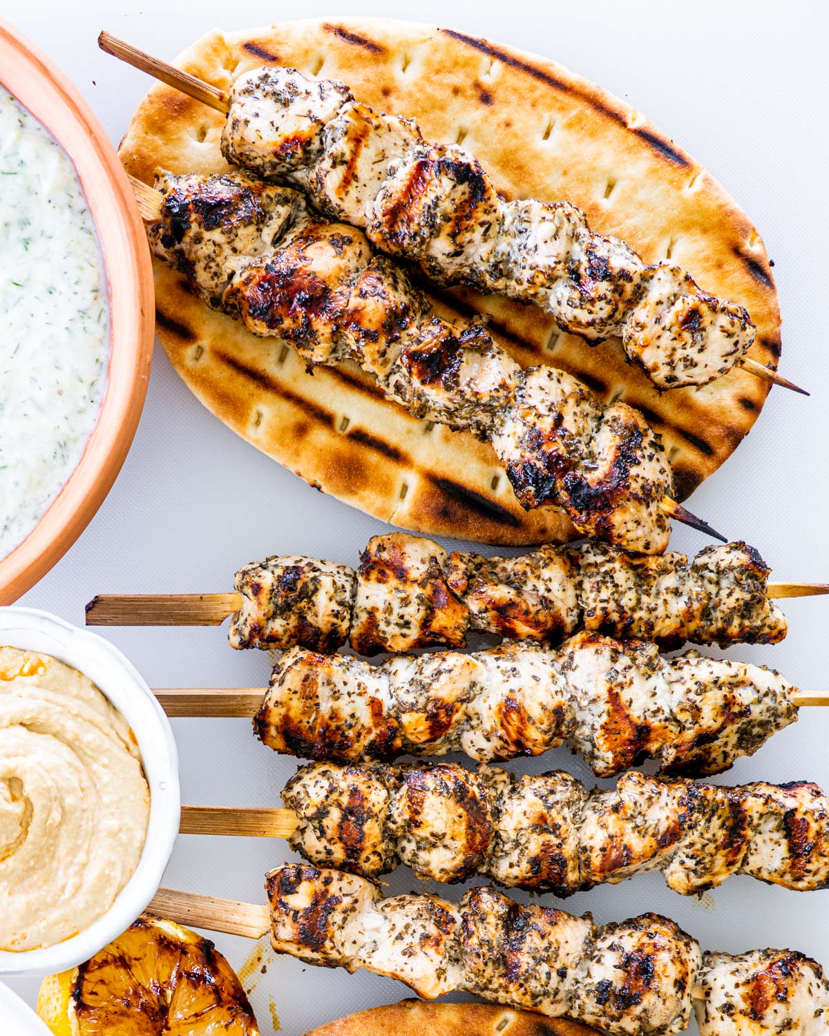 overhead shot of chicken souvlaki skewers with a couple skewers on a pita bread