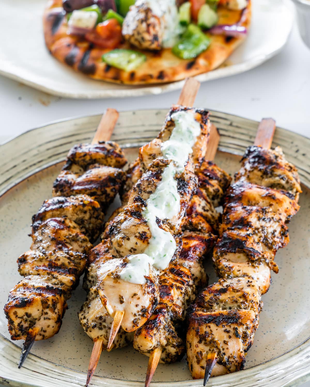 side view shot chicken souvlaki skewers with a little tzatziki on a plate