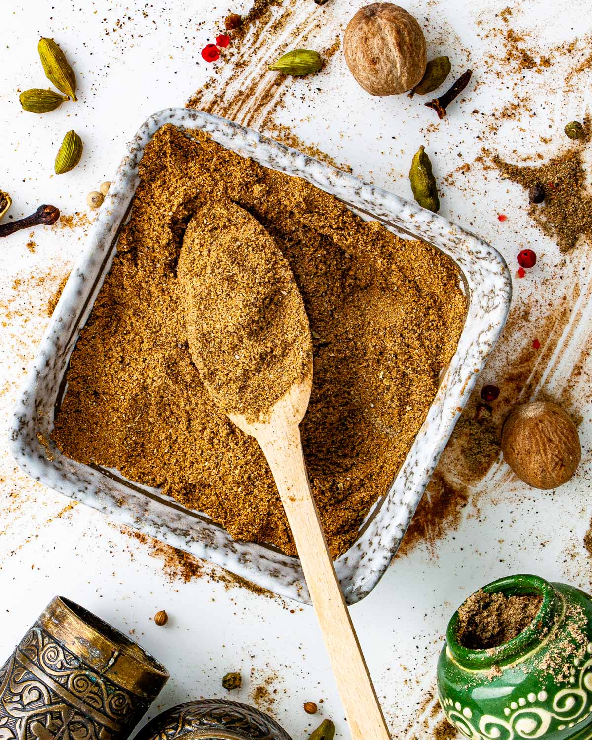overhead shot of a square bowl filled with garam masala and a mini wooden spoon inside