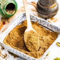 a square bowl filled with garam masala and a mini wooden spoon inside