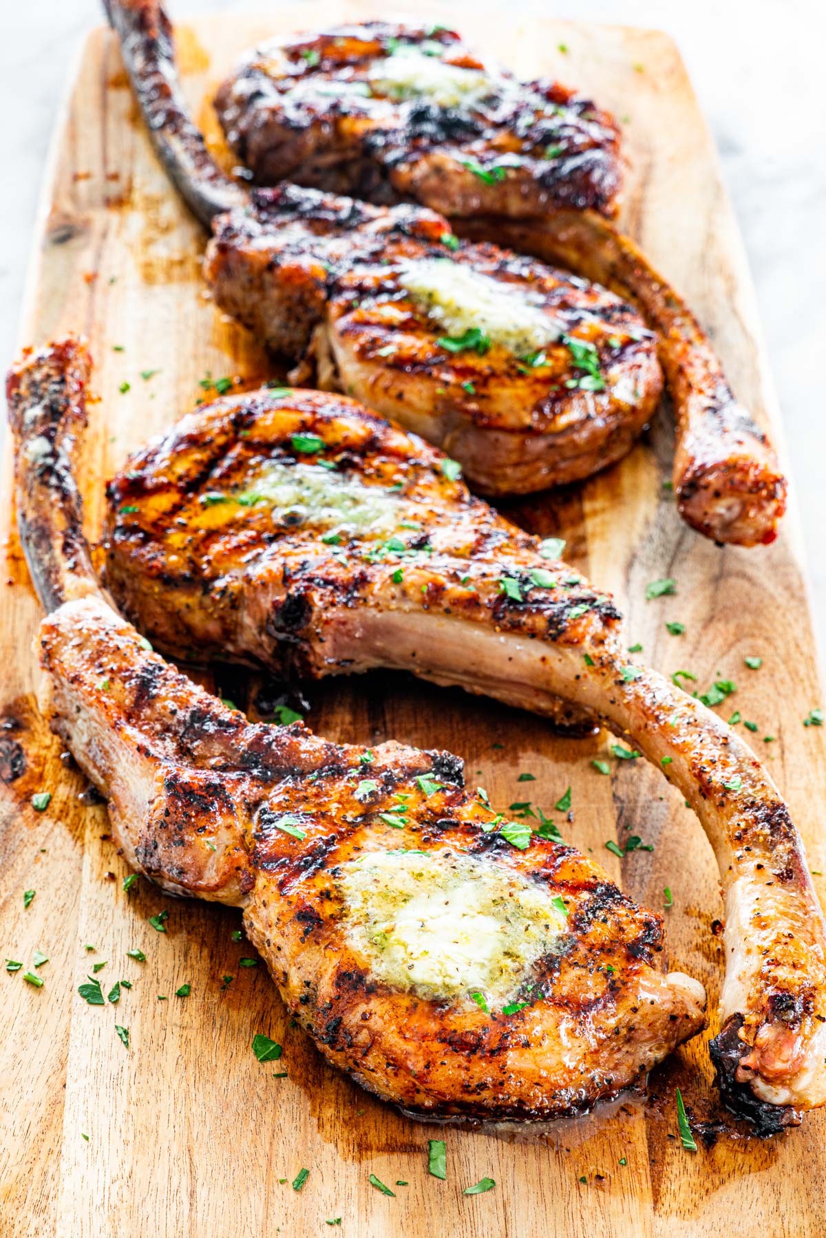 side view shot of tomahawk pork chops grilled to perfection with a pat of compound butter on each on a cutting board