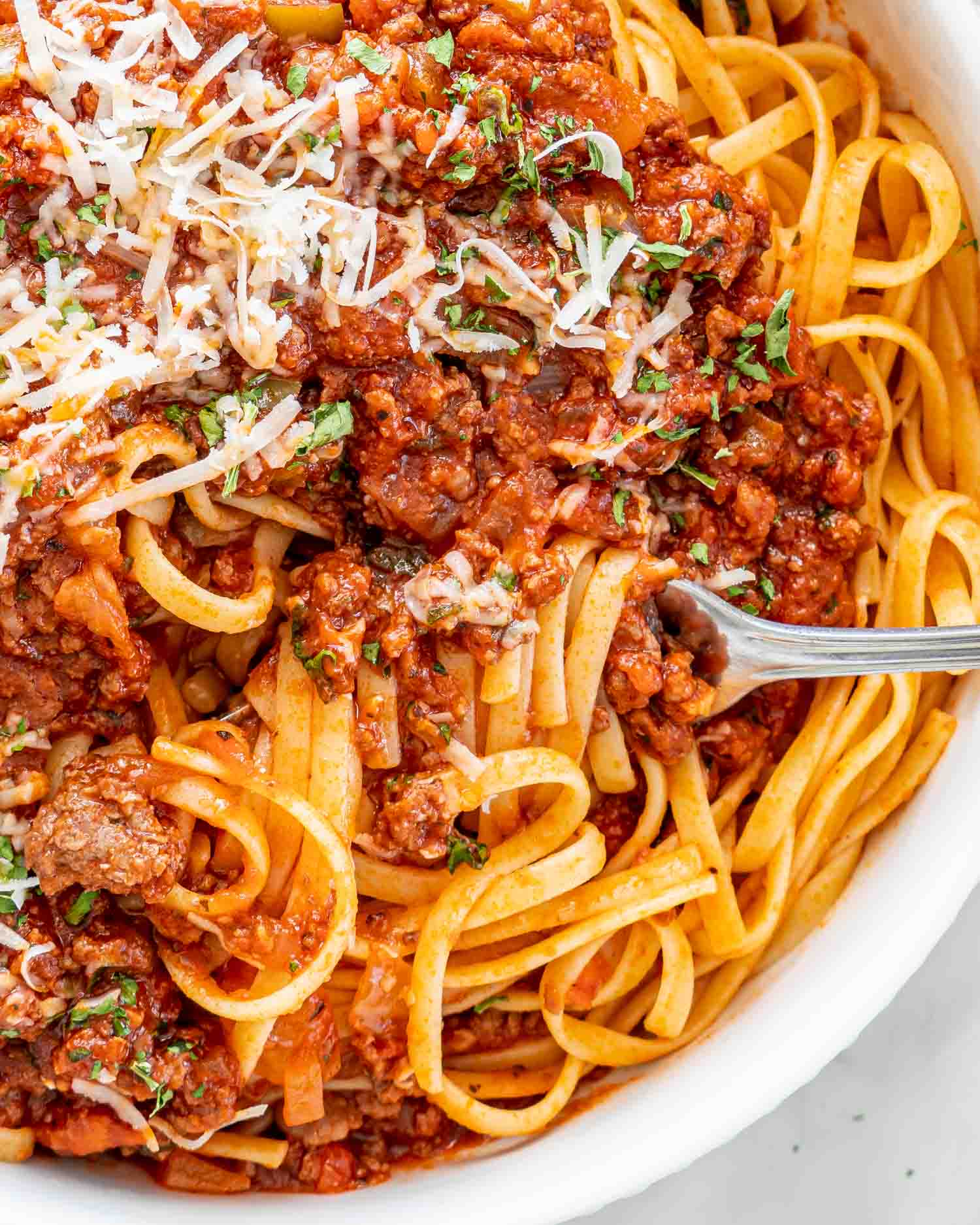 meat sauce over a bed of linguini with a fork twisting some pasta garnished with parmesan cheese and parsley