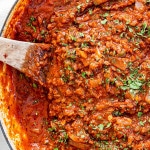 meat sauce in a braiser with a wooden spoon in it and garnished with parsley