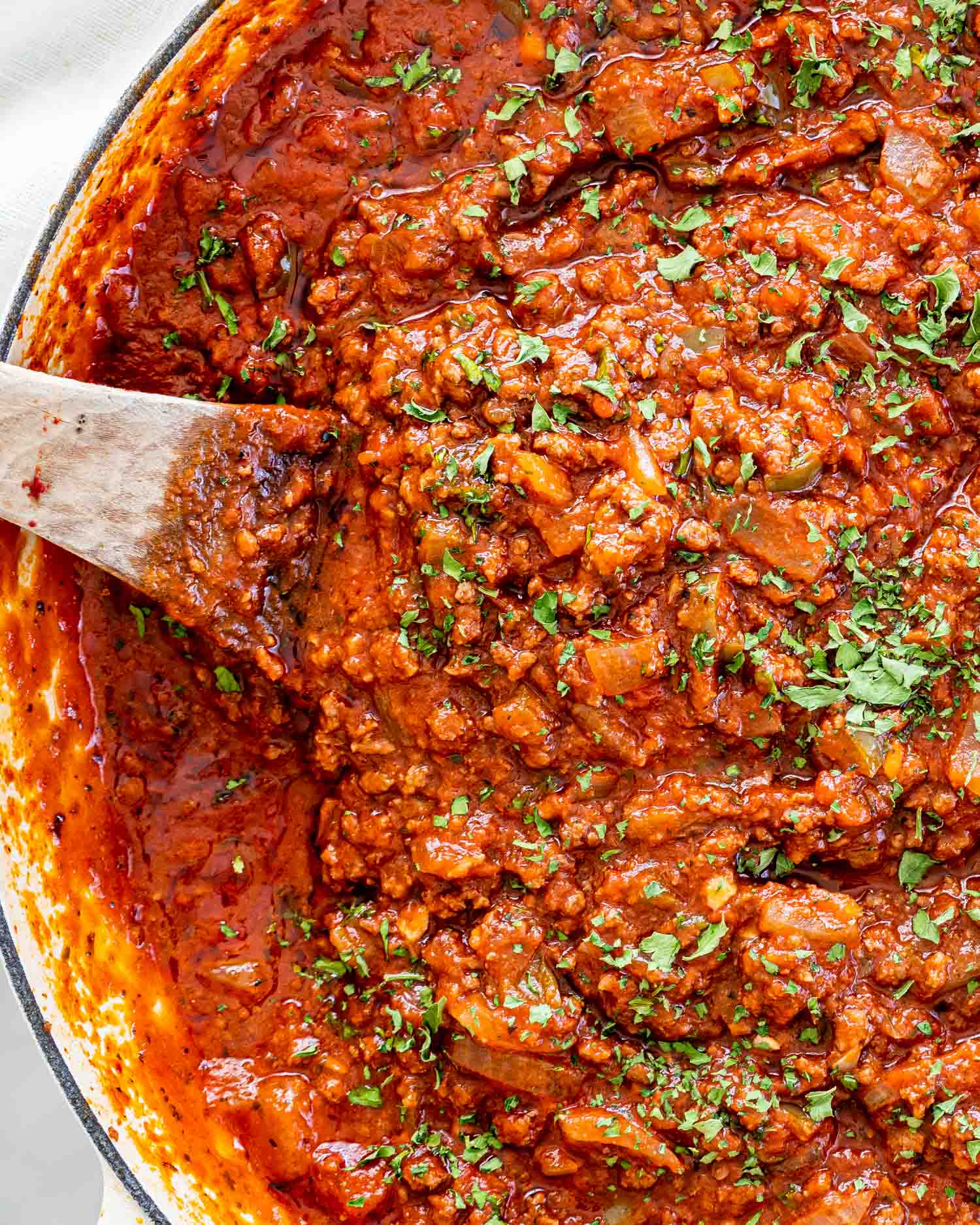 meat sauce in a braiser with a wooden spoon in it and garnished with parsley