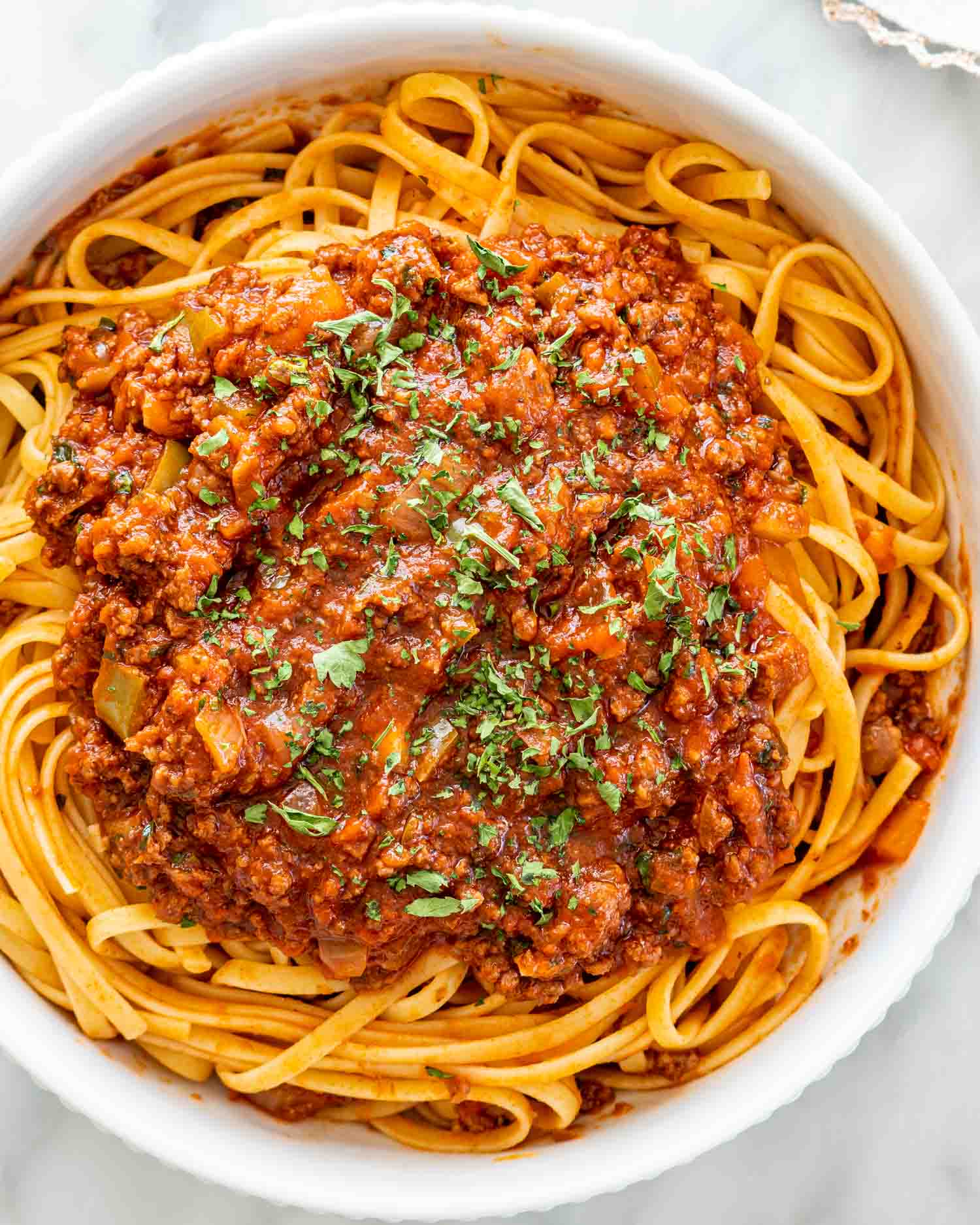 linguini in a white bowl with lots of meat sauce and garnished with parsley