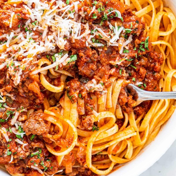 overhead closeup shot of meat sauce over a bed of linguini with a fork twisting some pasta garnished with parmesan cheese and parsley