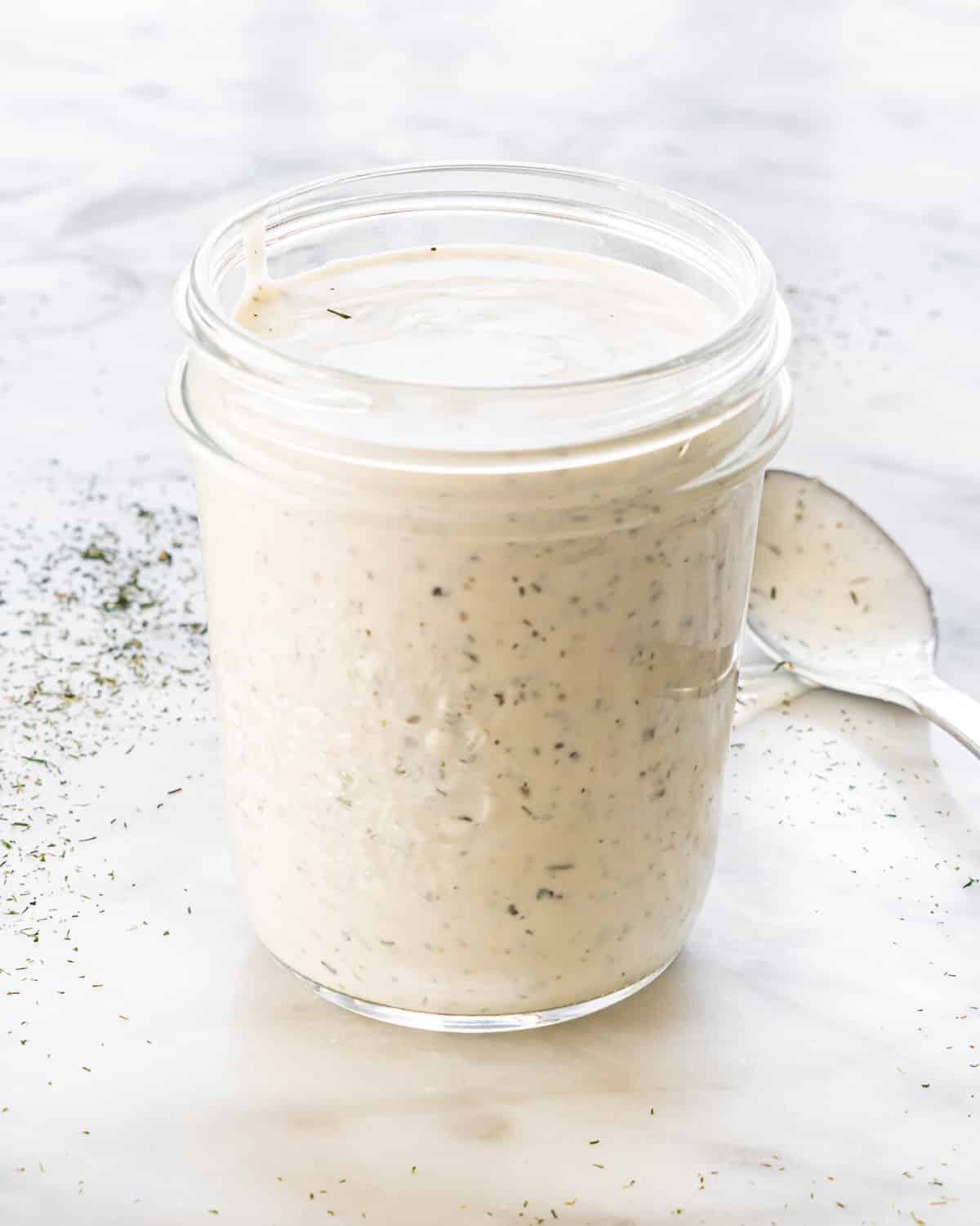 side view shot of a jar filled with homemade ranch dressing and a spoon next to it