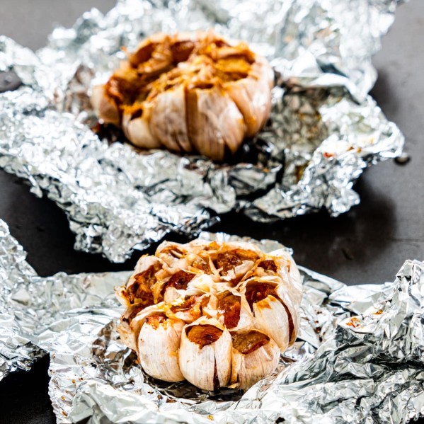 two head of roasted garlic in aluminum foil on a baking sheet