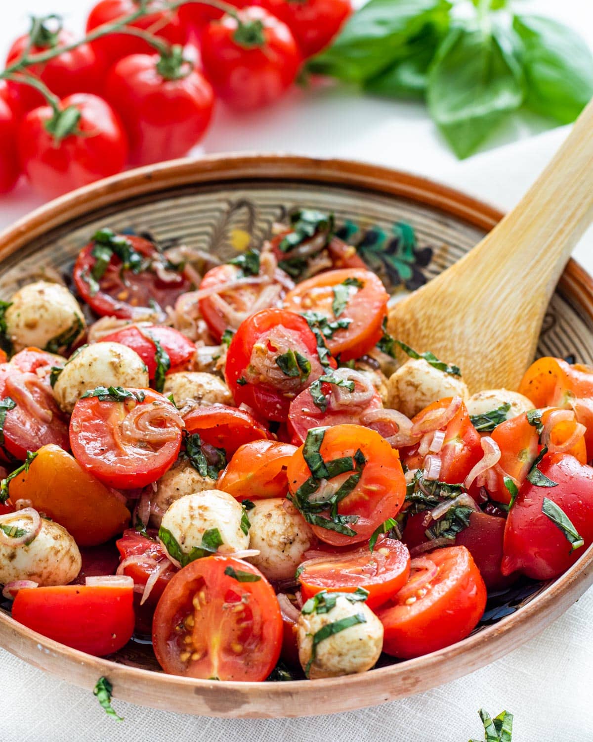 tomato basil salad in a small serving bowl with a serving spoon in it