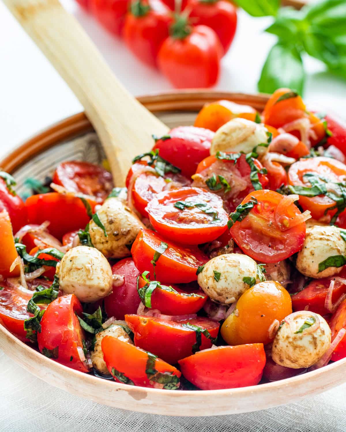 tomato basil salad in a small serving bowl with a serving spoon in it