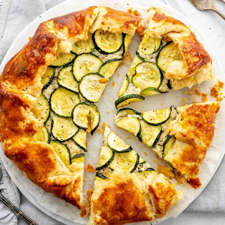 a zucchini ricotta galette on a white plate cut into slices.