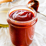 homemade bbq sauce in a jar with a ladle behind it