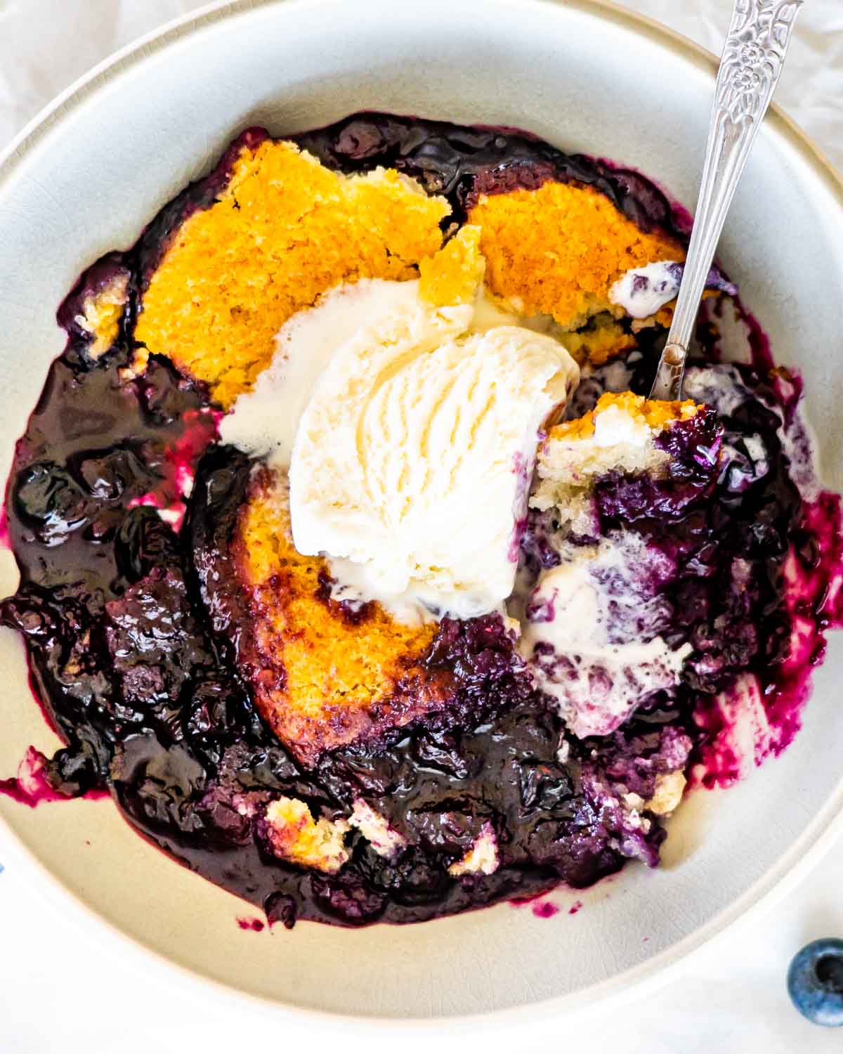 overhead shot of a blueberry cobbler in a bowl with a scoop of vanilla ice cream