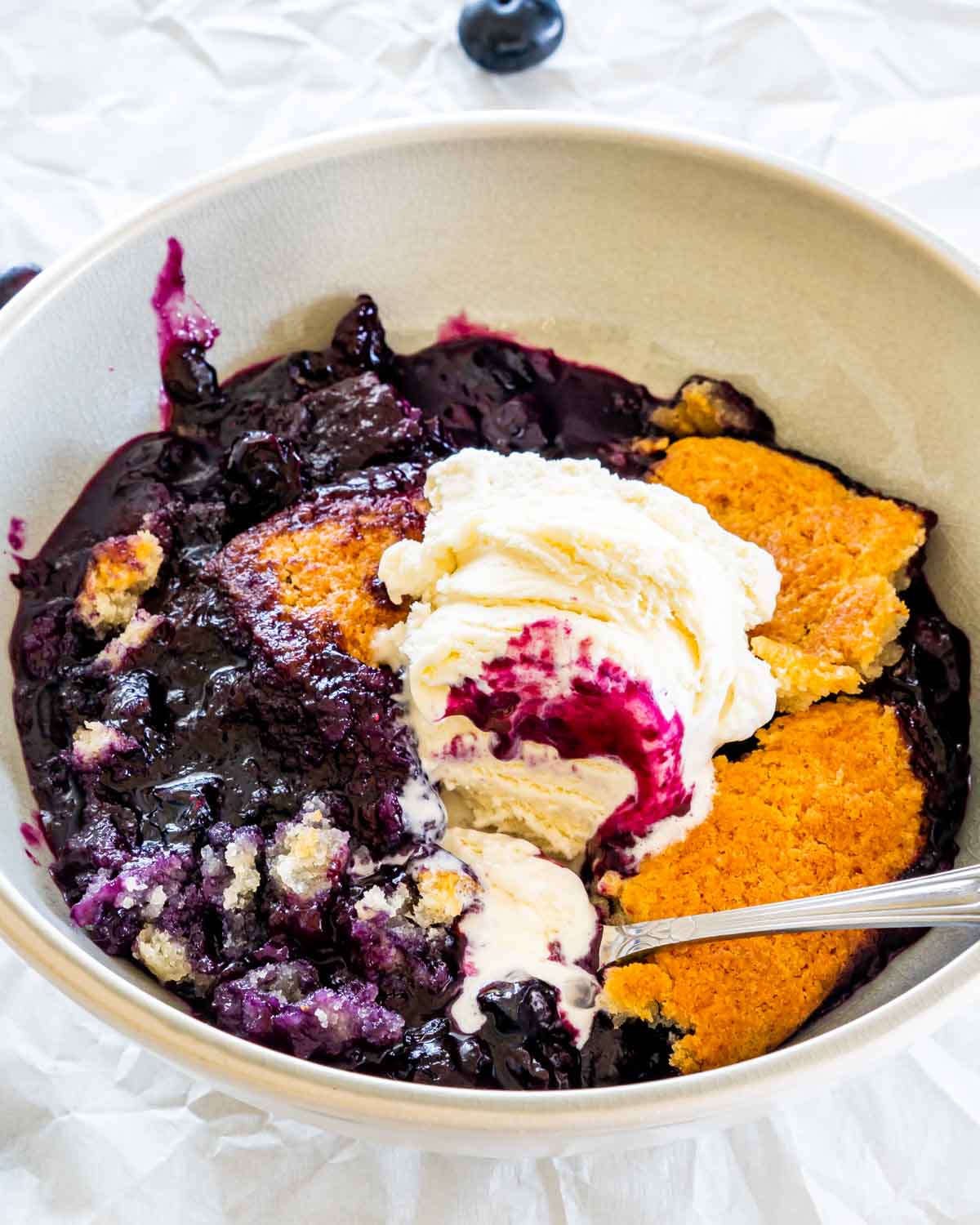 sideview shot of a blueberry cobbler in a bowl with a scoop of vanilla ice cream