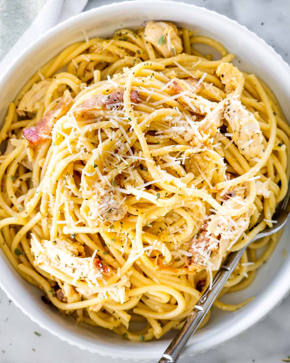 overhead shot of chicken carbonara in a white bowl with a fork and garnished with parmesan cheese