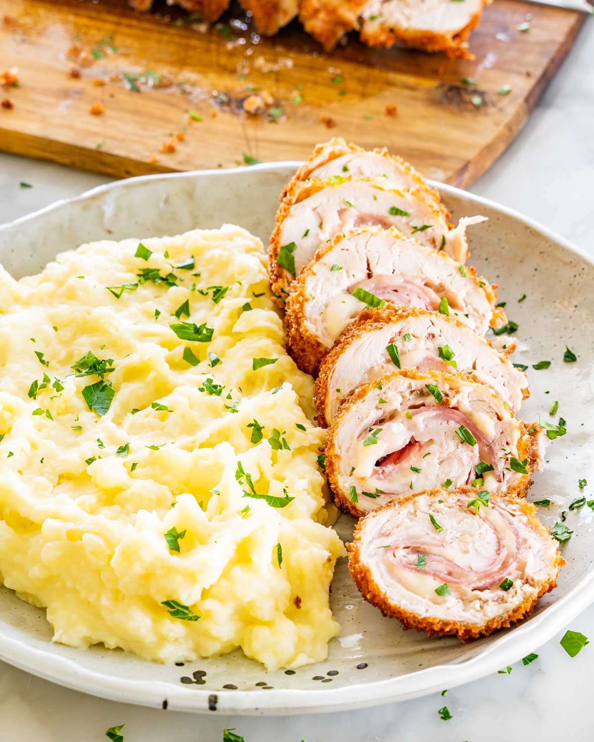 side view shot of chicken cordon bleu next to a side of mashed potatoes.