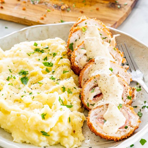 sliced up chicken cordon-bleu with sauce on a plate with mashed potatoes.