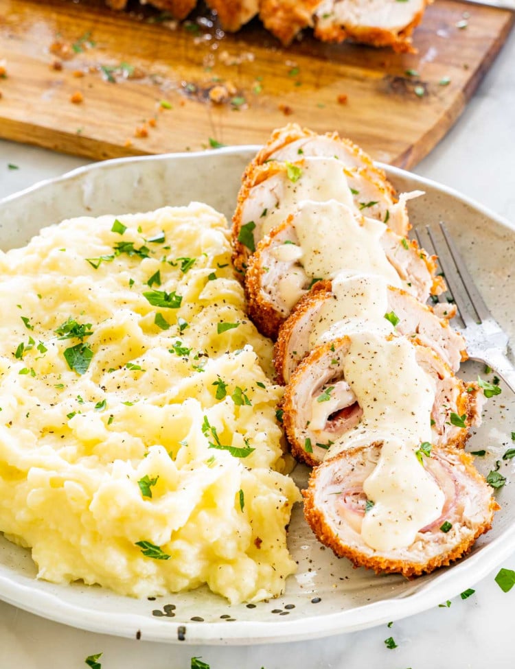 sliced up chicken cordon-bleu with sauce on a plate with mashed potatoes.