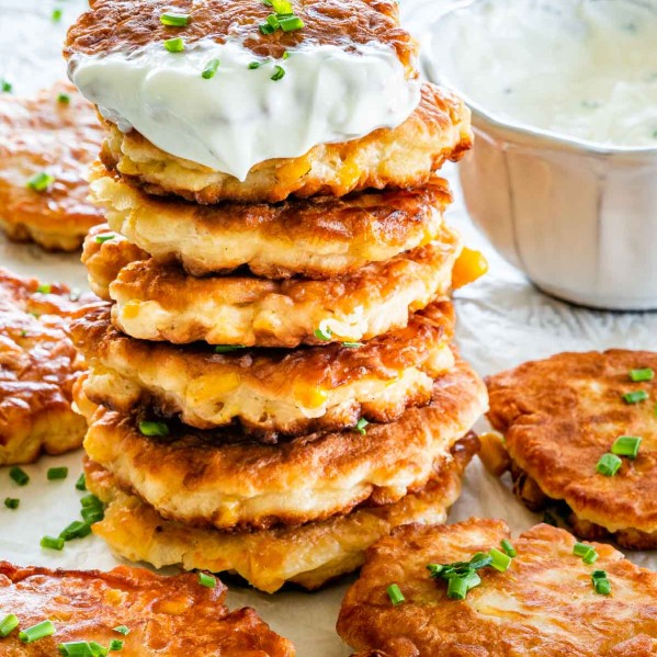 a stack of corn fritters garnished with some chives and a little bowl of sour cream in the background