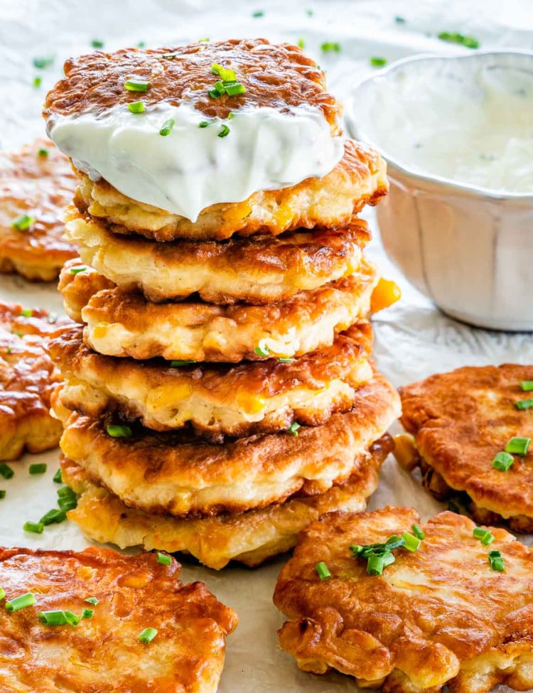 a stack of corn fritters garnished with some chives and a little bowl of sour cream in the background