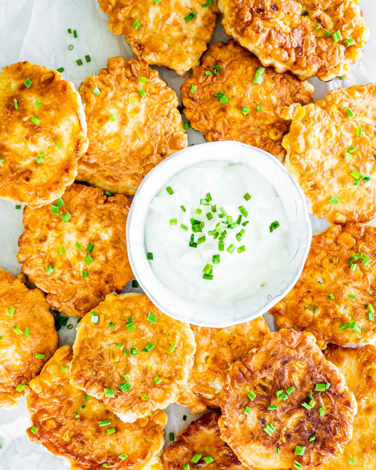 overhead shot of a bowl filled with sour cream surrounded but a bunch of corn fritters