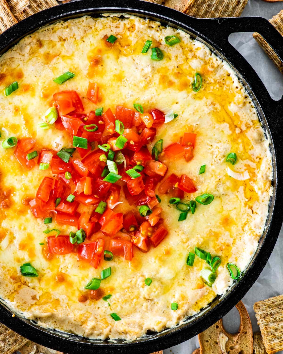 overhead shot of hot cheesy crab dip fresh from the oven and topped with freshly chopped tomatoes and green onions