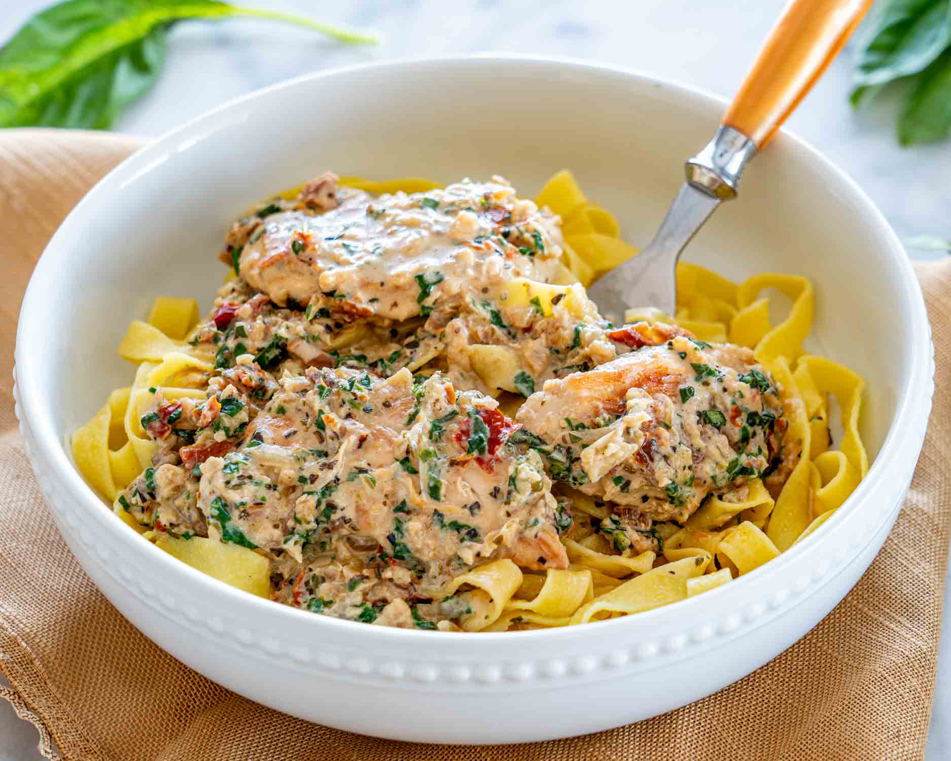 overhead shot of creamy tuscan chicken over a plate of noodles.
