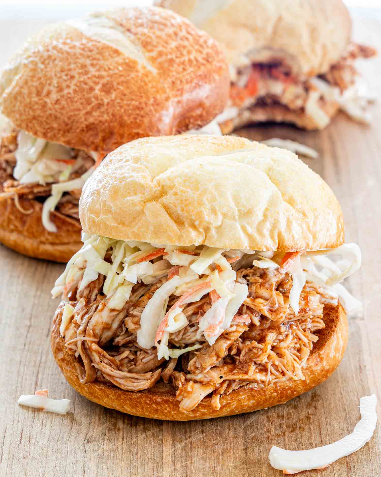 side view shot of a bbq pulled chicken sandwich with coleslaw on a cutting board.