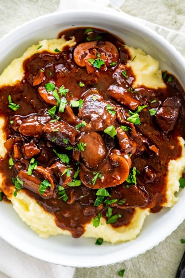 overhead shot of beef burgundy over a bed of mashed potatoes garnished with parsley in a white plate