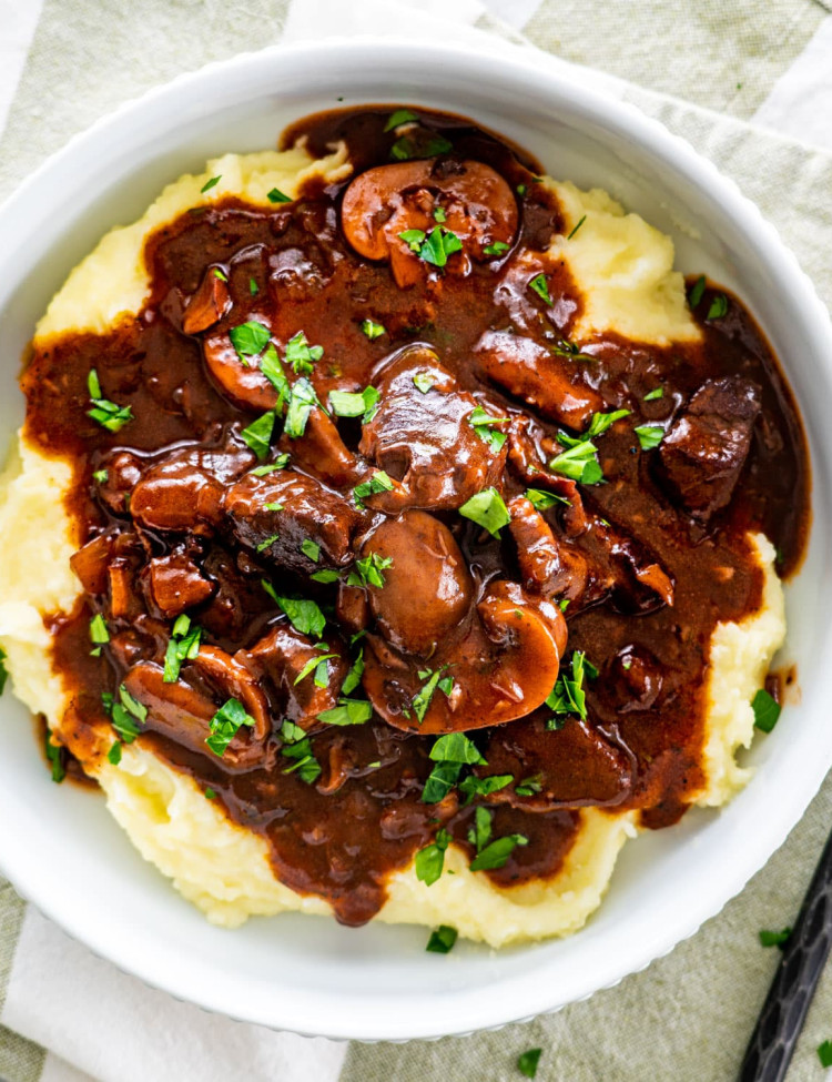 overhead shot of beef burgundy over a bed of mashed potatoes garnished with parsley in a white plate