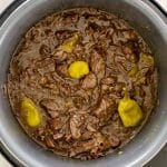 Mississippi pot roast cooking inside Instant Pot, surrounded by pepperoncini and sauce, ready to shred into tender pieces.